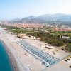 Veduta aerea di una lunga spiaggia con ombrelloni e una città sullo sfondo.
