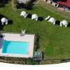 Vista dall'alto di una piscina con sdraio e ombrelloni su prato.