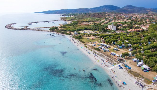 Spiaggia con sabbia chiara e mare cristallino, montagne sullo sfondo.