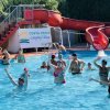 Persone in una piscina vicino a uno scivolo rosso, un cartello delinea il nome del villaggio.