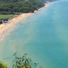 Lunga spiaggia vista dall'alto, con mare turchese e colline verdi sullo sfondo.