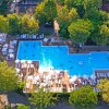 Piscina grande a forma irregolare circondata da ombrelloni e lettini, immersa nel verde.
