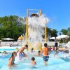 Bambini giocano sotto un grosso secchio d'acqua in una piscina all'aperto.