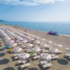 Spiaggia con file di ombrelloni bianchi e mare calmo.