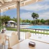Tavoli di un ristorante con vista su una piscina blu e alberi circostanti.