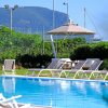 Una piscina con lettini e un ombrellone, circondata da vegetazione e montagne.