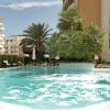 Piscina all'aperto con palme al centro, circondata da edifici e sedie a sdraio.