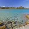 Spiaggia con acqua cristallina e sfondo montuoso.