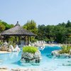Piscina con gazebo di paglia e sedie a sdraio tra piante tropicali.