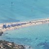 Spiaggia con ombrelloni blu, bagnanti e sport acquatici.