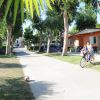 Persona con bambino in bici in un villaggio con alberi e case colorate.
