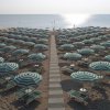 Spiaggia affollata con ombrelloni a righe verde e bianco, con passerella centrale verso il mare.