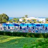 Ampia piscina con ombrelloni blu e lettini, vista mare e vegetazione circostante.