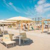 Spiaggia con lettini e ombrelloni bianchi, cielo azzurro e palazzi in lontananza.