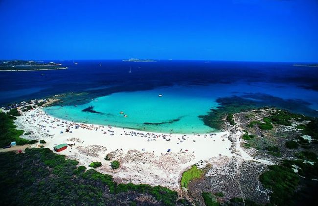 Una spiaggia con sabbia bianca e mare azzurro, circondata da una vegetazione verde.