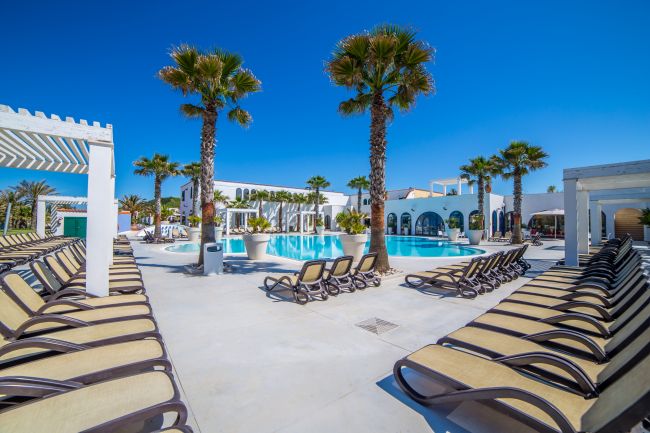 Piscina circondata da palme e lettini, sotto un cielo blu limpido.