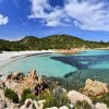 Una spiaggia con acque cristalline, rocce e colline verdi in lontananza.