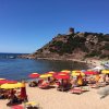Spiaggia con ombrelloni colorati, torre su collina sullo sfondo.