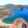 Baia con acqua cristallina, spiaggia bianca e vegetazione verde.