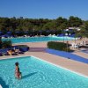 Piscina all'aperto con sdraio e ombrelloni, circondata da alberi e palme.
